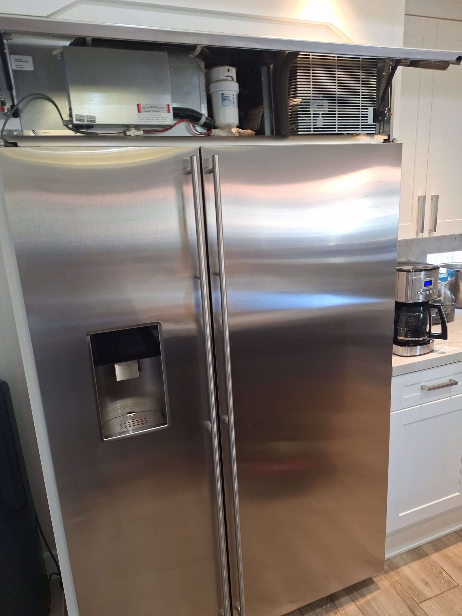 Built-in side-by-side refrigerator with its upper panel raised to expose the condenser and equipment compartment