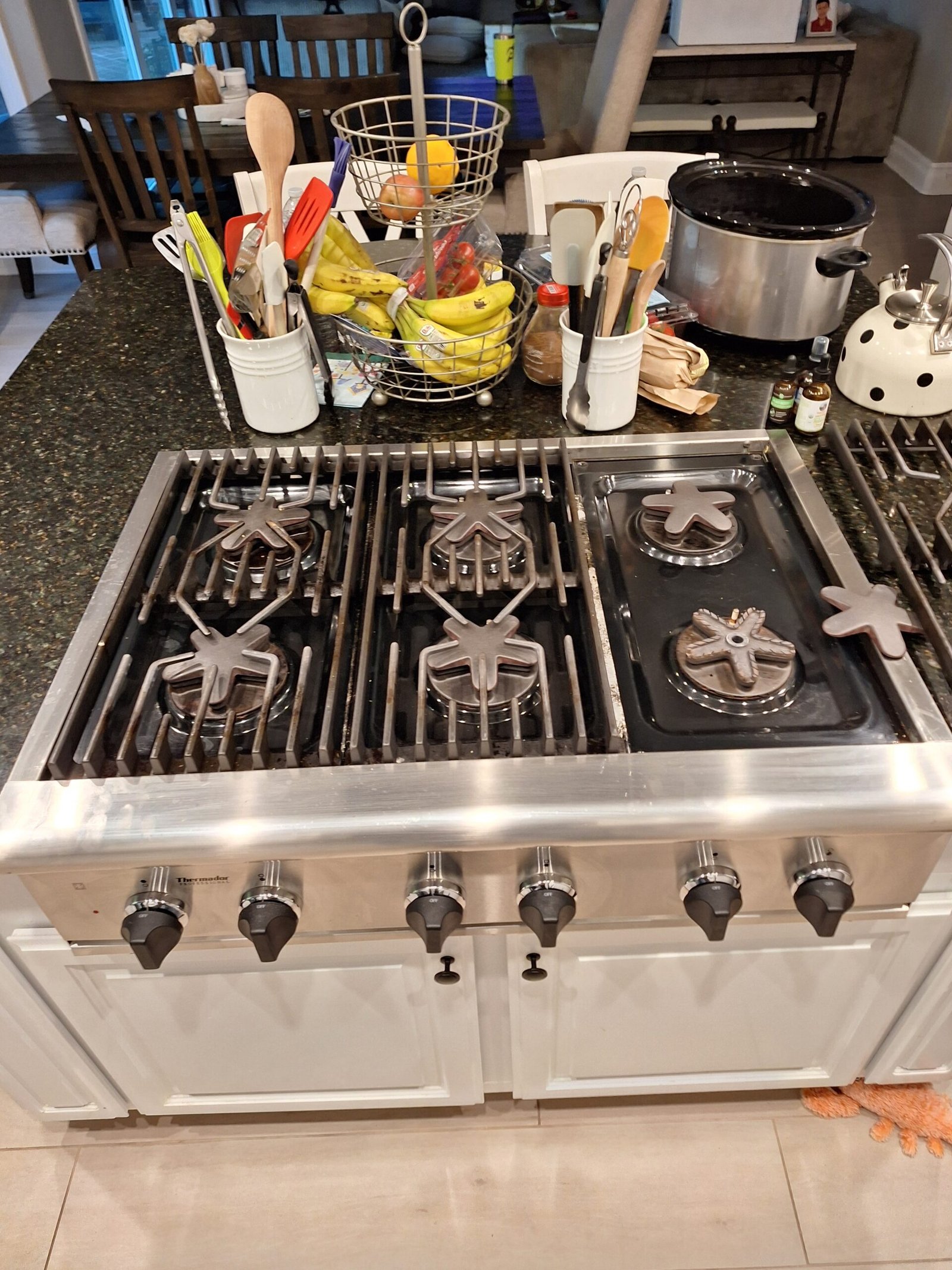 Six-burner stainless steel gas cooktop with star-shaped burner caps removed for access